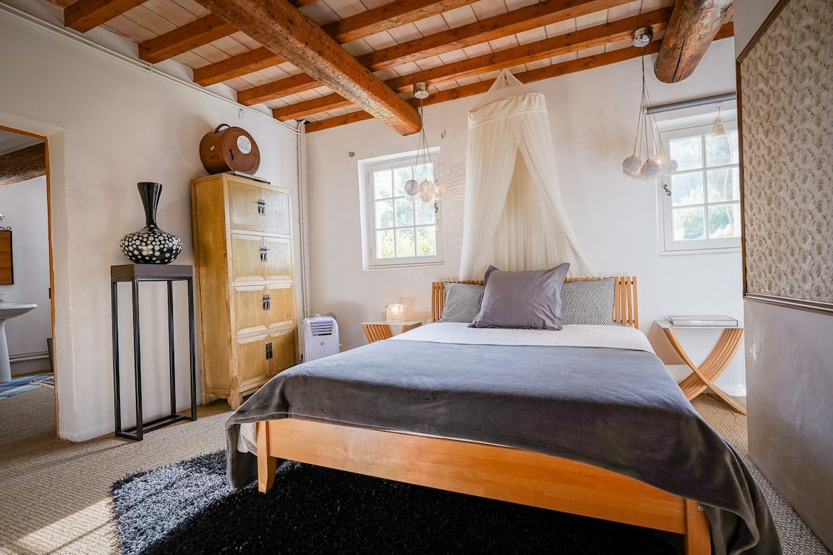 La chambre Orange, a bed below a beamed ceiling with a window onto the garden